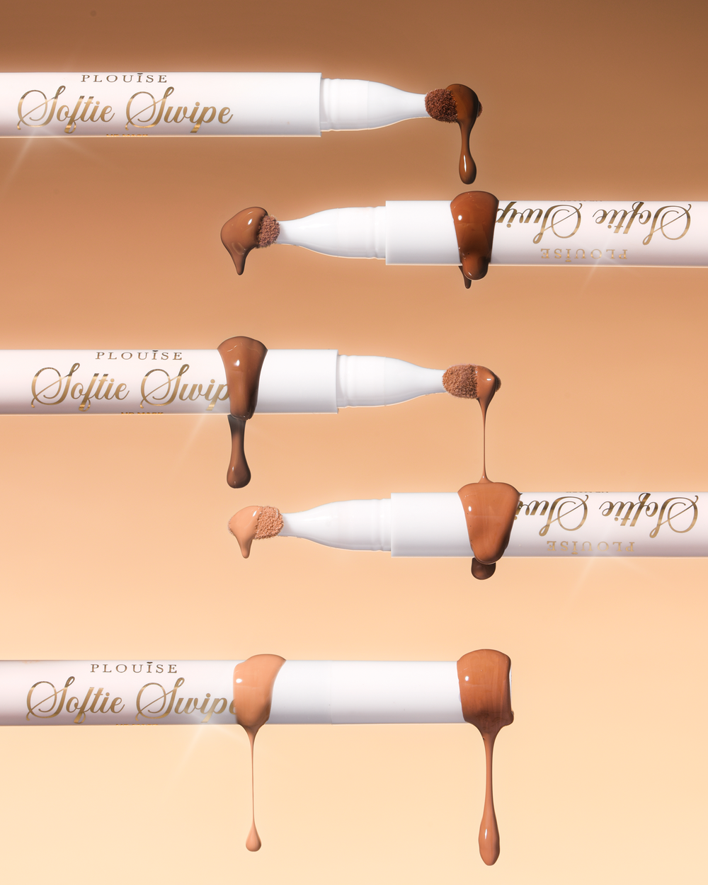 Una imagen de cinco mascarillas de labios teñidas Softie Swipe de P.Louise con producto goteando de las puntas que muestran los distintos tonos sobre un fondo beige.