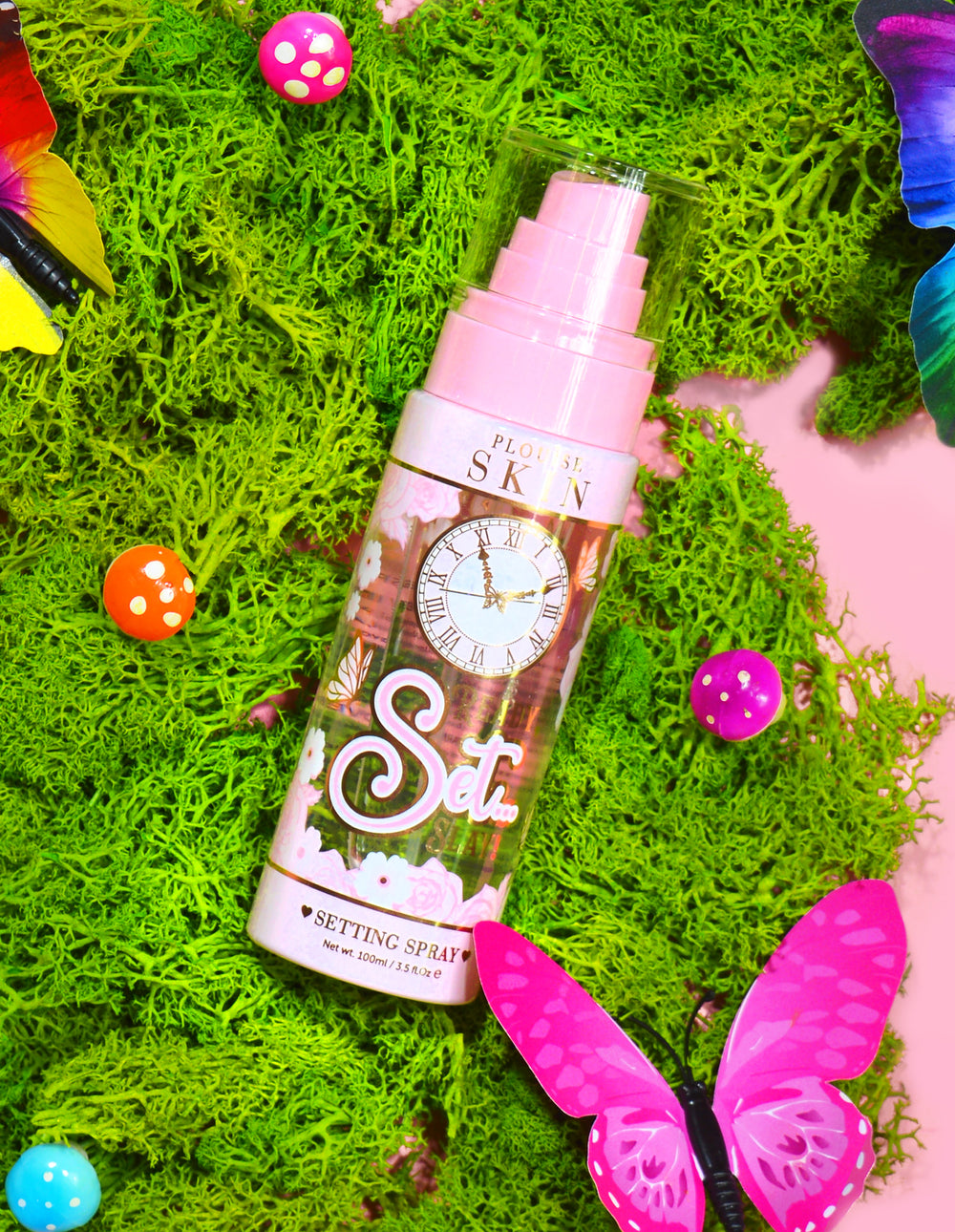 Una botella de spray fijador de larga duración Ready Set Slay de P. Louise rodeada de elementos decorativos que incluyen coloridos musgos artificiales, mariposas y hongos.