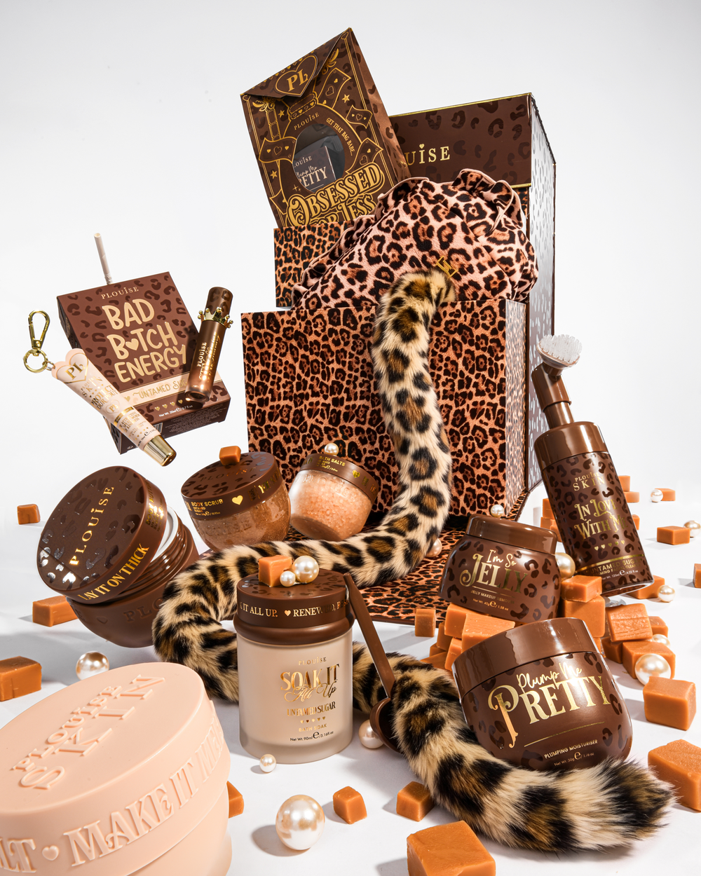 Et luksuriøst skønhedsgavesæt stylet med brune og leopardprint-elementer, inklusive en leopardprint-gavepose, en leopardprint-hale og flere kosmetikbeholdere i brune og beige toner, arrangeret på en hvid baggrund med karamelfarvede terninger og perler.
