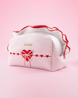 Un bolso de maquillaje y cuidado de la piel P.Louise a rayas rosas y blancas con volantes y un diseño de corazón sobre un fondo rosa