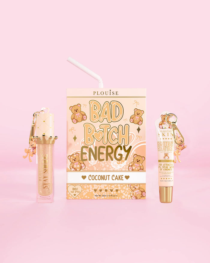 En P.Louise Teddy Glitter Bad Bitch Energy Lip Duo i kokosnøddekageduft med læbebalsam og læbeolie på en lyserød baggrund
