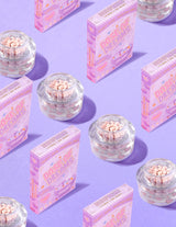 Klare beholdere med P.Louise DOse of Dreams Vitamin C Capsule Face Cream med pink kapsel i omgivet af lyserøde kornkasser på en lilla baggrund