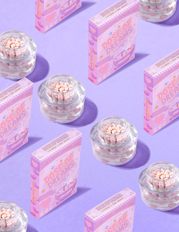 Klare beholdere med P.Louise DOse of Dreams Vitamin C Capsule Face Cream med pink kapsel i omgivet af lyserøde kornkasser på en lilla baggrund