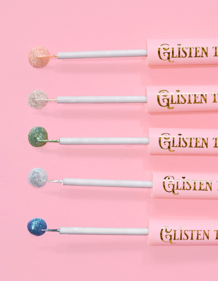5 P.Louise Glisten To Your Heart glitter eyeliners linet op med et dryp af produktet på enden mod en lyserød baggrund