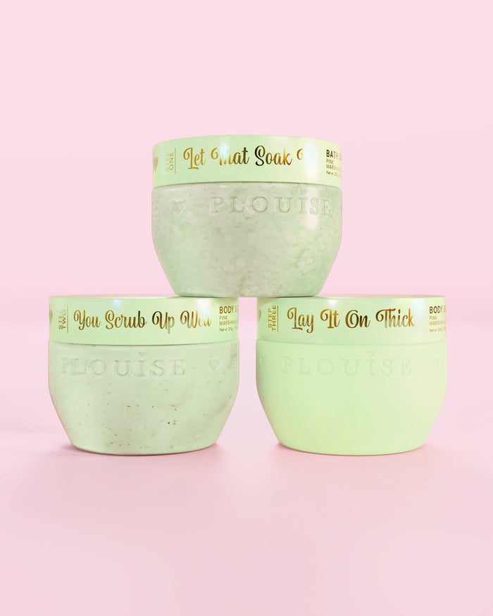 Tre P.Louise Hop Into Self-Care Chokolade Dækkede Jordbær grønne beholdere med badesalte, bodyscrub og body butter med guldtekst på en lyserød baggrund