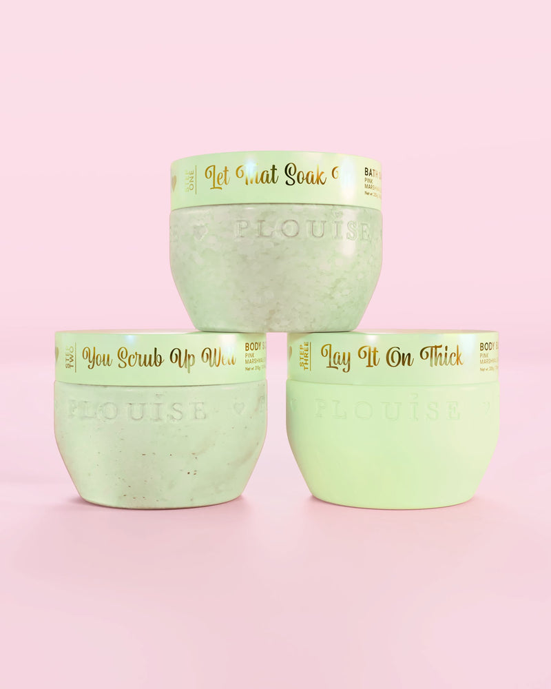 Tre P.Louise Hop Into Self-Care Chokolade Dækkede Jordbær grønne beholdere med badesalte, bodyscrub og body butter med guldtekst på en lyserød baggrund