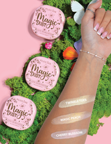 Tres resaltadores sueltos compactos con la etiqueta Magic Dust en los tonos Twinkle Toes, Magic Peach y Cherry Blossom, exhibidos en un brazo con un fondo floral.