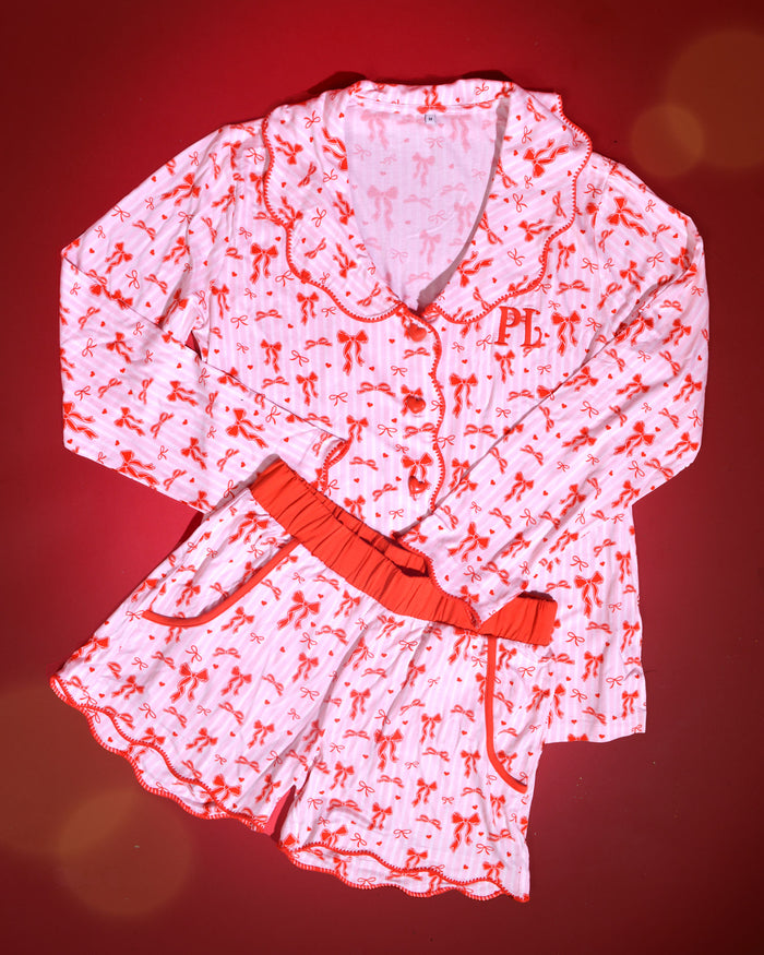Billede af pink og hvidstribet julepyjamas for voksne med rød sløjfedesign på en rød baggrund