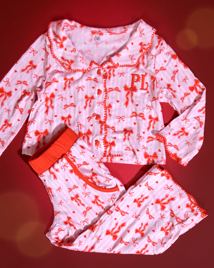Conjunto de pijamas navideños para niños de rayas rosas y blancas con diseños de lazos rojos sobre un fondo rojo
