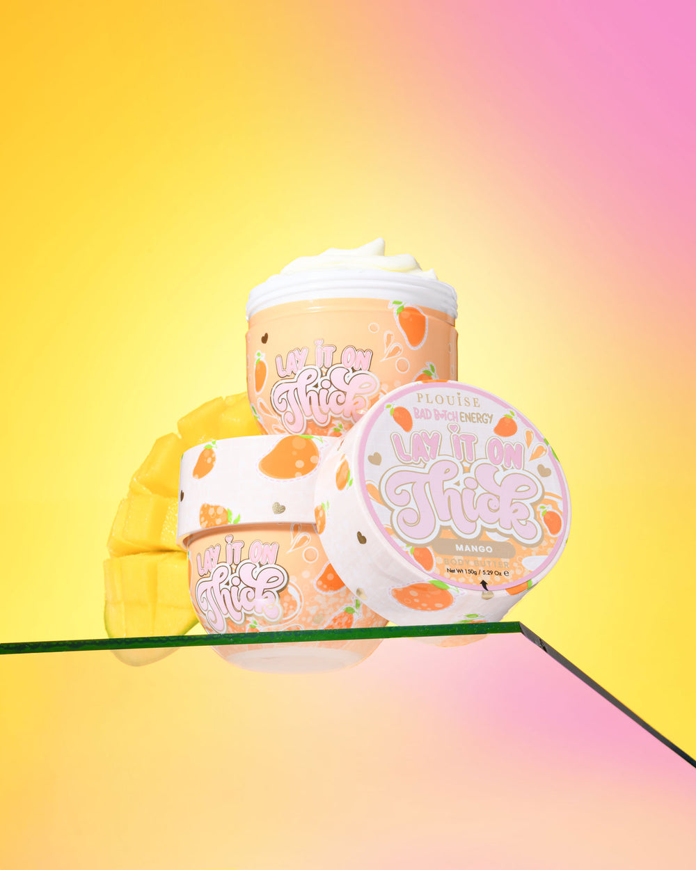 Tres recipientes de manteca corporal de mango P. Louise 'Lift It On Thick' sobre un fondo amarillo y rosa degradado
