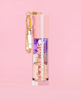 P. Louise Soak Me Lip Oil con aceite en capas de colores en un tubo rosa con un cierre dorado sobre un fondo rosa