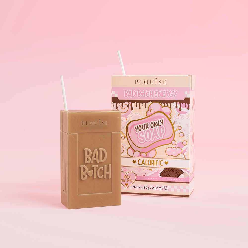 Una pastilla de jabón marrón con la inscripción 'Bad Bitch' grabada, acompañada de una colorida caja de jugo con la etiqueta 'Calorific', presentada sobre un fondo rosa.