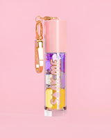 P. Louise Soak Me Lip Oil con aceite en capas de colores en un tubo rosa con un cierre dorado sobre un fondo rosa